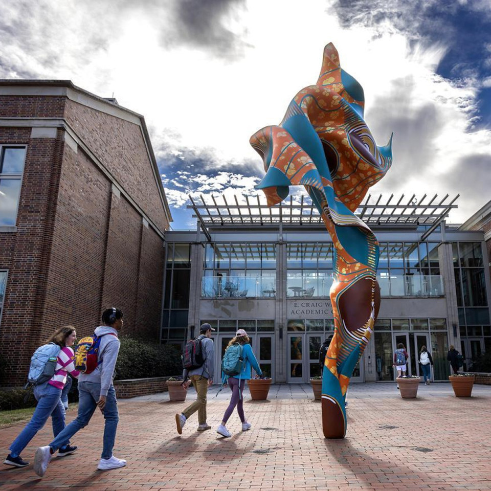 Four students walking across brick pathway to the left of a twisting sculpture